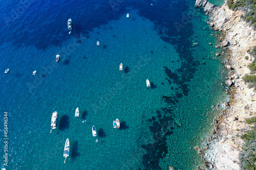 View from above, stunning aerial view of a bay with boats and luxury yachts sailing on a turquoise, clear water. Porto Santo Stefano, Italy.