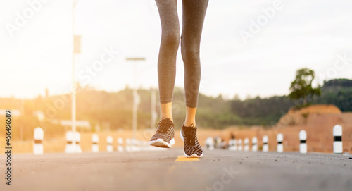 Close up athlete Asian young girl running exercise warming stretching legs fitness training healthy lifestyle, wearing runner sport shoes, jogging on tarmac street road morning sunrise outdoor
