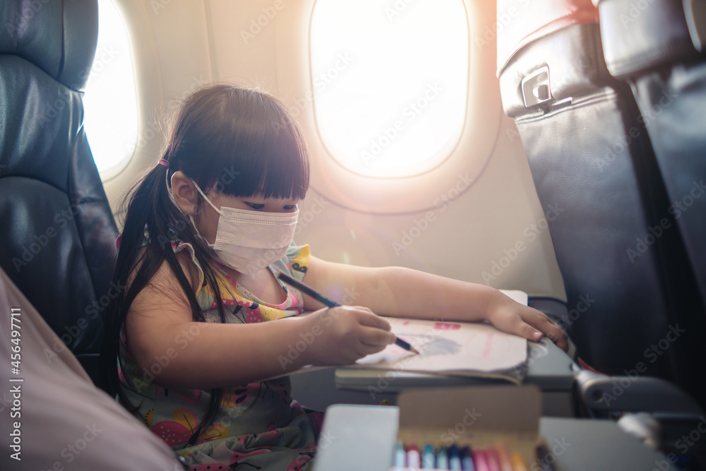 Obraz premium Adorable Asian young girl traveling commuting on plane transportation wearing surgical facemask protection from COVID-19 coronavirus, commercial airline services, happy joyful in evening sunset.