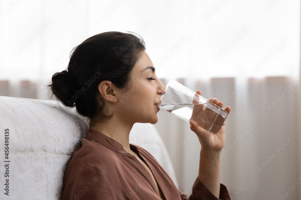 Drinking water. Side view young indian woman enjoy pure fresh cool mineral water at morning. Profile shot of thirsty millennial mixed race lady hold glass swallow crystal still aqua with closed eyes Drinking water. Side view young indian woman enjoy pure fresh cool mineral water at morning. Profile shot of thirsty millennial mixed race lady hold glass swallow crystal still aqua with closed eyes