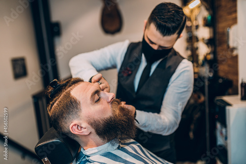 Good looking hipster young bearded man visiting hairstylist in barber shop.