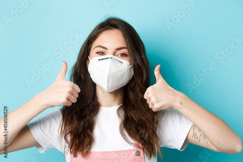 Covid-19, social distancing and lockdown concept. Close up of young woman in respirator showing thumbs up, smiling and nod in approval, protect herself from coronavirus during quarantine photo