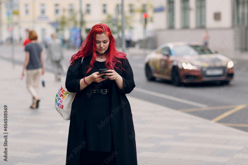 Fototapeta premium European plus size woman walking outdoor street city with mobile cellular phone. Young red pink haired body positive girl using cellphone smartphone