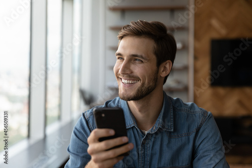 Overjoyed millennial Caucasian man use cellphone talk speak on video call on modern gadget. Smiling young male look in distance hold smartphone have webcam virtual communication. Technology concept.