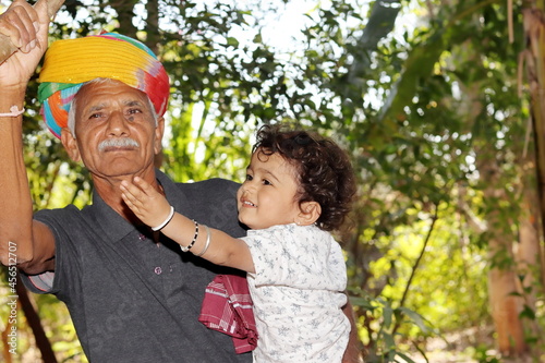 Close-up portrait of A small Indian son to Asian elderly grandfather looks up at the fruit in the garden with his hand pointing and wearing traditional dress like colourful turban