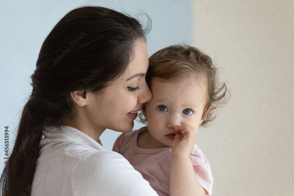 Happy beautiful new mom holding cute toddler baby in arms, smiling, kissing little kid with love, tenderness. Mother hugging, cuddling infant child, enjoying maternity leave after childbirth. Close up Happy beautiful new mom holding cute toddler baby in arms, smiling, kissing little kid with love, tenderness. Mother hugging, cuddling infant child, enjoying maternity leave after childbirth. Close up