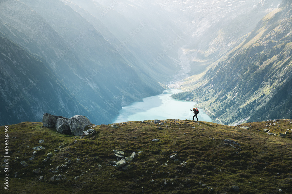 Splending view of a female climber hiking over mountain ridge against blue, turquoise lake in Zillertal Alps, Austria