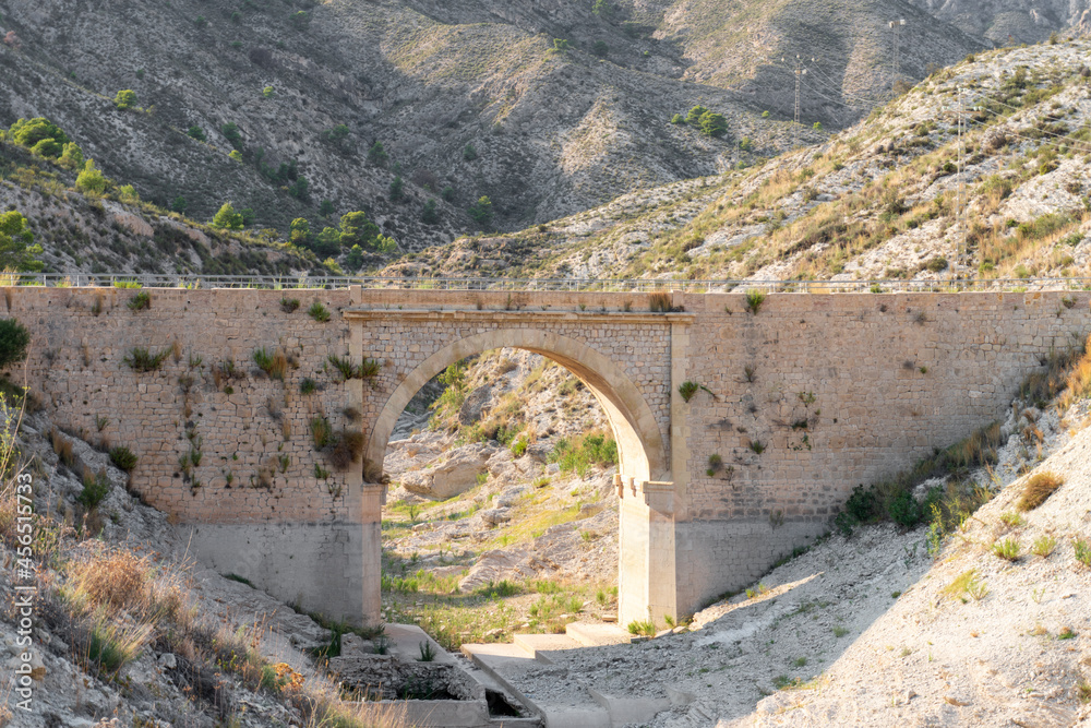 Small brick and masonry bridge over a dry riverbed surrounded by mountains. Drought concept. 
