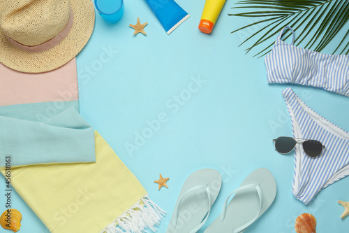 Frame of towel and different beach accessories on light blue background, flat lay. Space for text