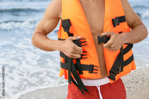 Lifeguard putting on life vest near sea, closeup