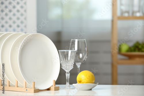 Clean plates in dish drying rack, glasses and lemon on white table indoors photo