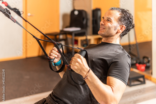 Fototapeta Naklejka Na Ścianę i Meble -  Athlete man doing exercise with fitness straps at gym
