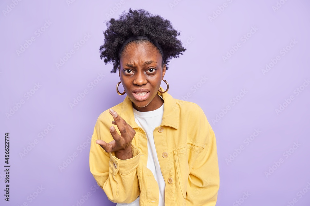 Displeased annoyed dark skinned woman gestures angrily looks indignant wears yellow jacket poses against purple background skeptically expresses disagreement being disappointed with final results Displeased annoyed dark skinned woman gestures angrily looks indignant wears yellow jacket poses against purple background skeptically expresses disagreement being disappointed with final results