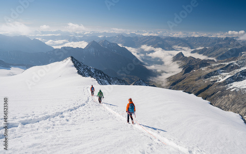 Climbers team on a trail through a dangerous glacier and avalanches in Austiran Alps. Epic moment near the top of Großvenediger glacier as the clouds disappear for a moment.