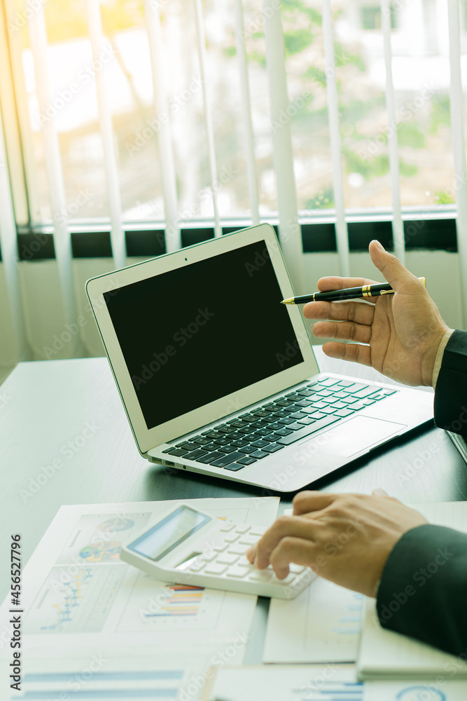 Young businessman analyzing business graph documents on desk with laptop computer and calculator Business and economic concepts with vertical images. Young businessman analyzing business graph documents on desk with laptop computer and calculator Business and economic concepts with vertical images.