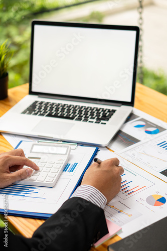 Young businessman analyzing business graph documents on desk with laptop computer and calculator Business and economic concepts with vertical images.