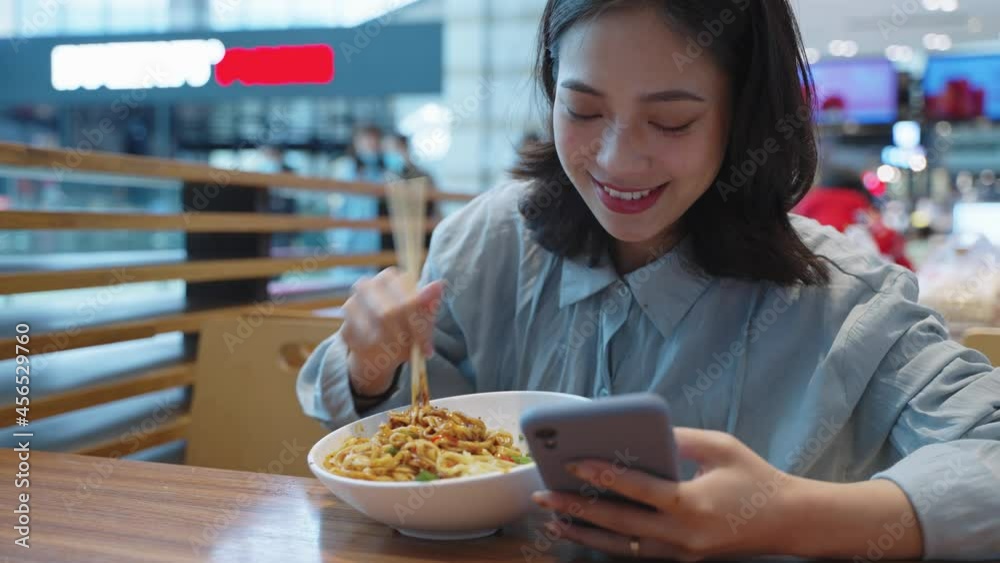4k clip of happy asian woman having lunch using chopsticks eating noodle looking at mobile phone in the restaurant 4k clip of happy asian woman having lunch using chopsticks eating noodle looking at mobile phone in the restaurant