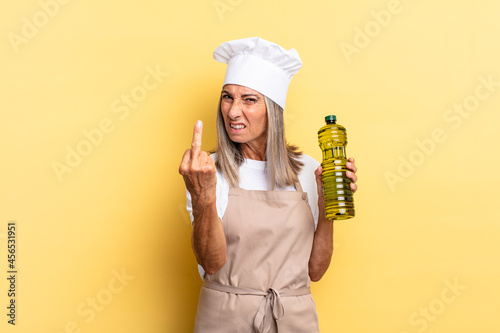 middle age chef woman feeling angry, annoyed, rebellious and aggressive, flipping the middle finger, fighting back