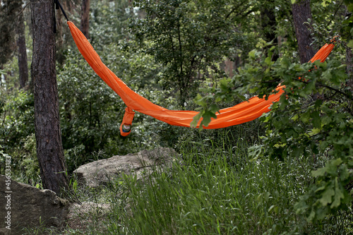 Bright orange hammock in nature. Relaxation and meditation concept. Rest and travel in the green forest. Summer or warm autumn