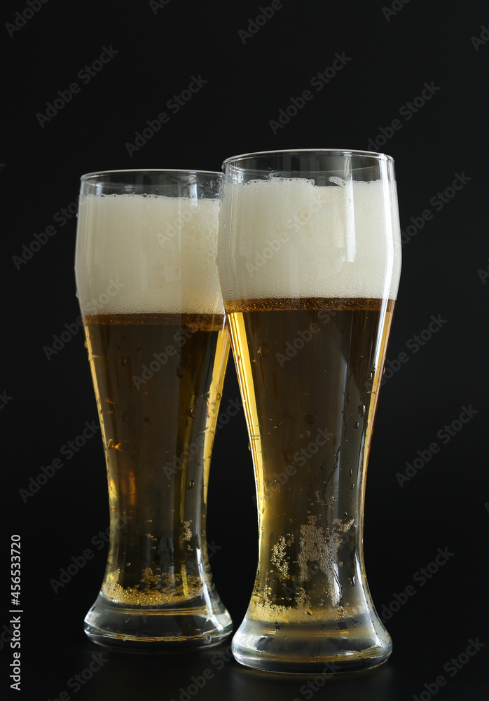 Two frosty glasses of cold golden beer with bubbles on the black background. Drinking alcohol on party, holidays, Oktoberfest or St. Patrick's Day.