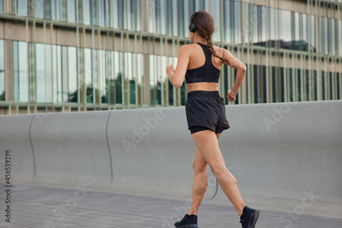 Outdoor shot of active slim woman has jog exercises being physically active covers long distance wants to come first at finish dressed in sportswear has morning workout. Back view of female jogger