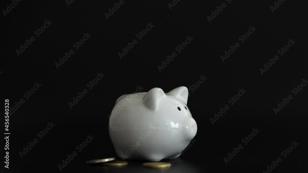 Hand putting money coin into piggy bank for saving money. Wealth, budget, investment, finance concept. Money box, piggybank on the black background Hand putting money coin into piggy bank for saving money. Wealth, budget, investment, finance concept. Money box, piggybank on the black background