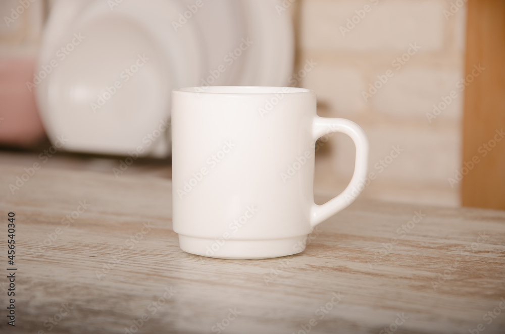 a white cup stands on a wooden table against a background of blurred plates with space for a logo or advertisement a white cup stands on a wooden table against a background of blurred plates with space for a logo or advertisement