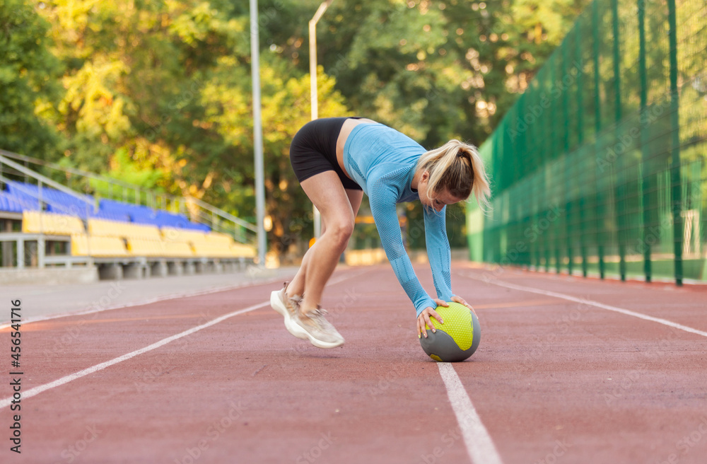 Athletic woman exercising in dynamics on medicine balls at the stadium