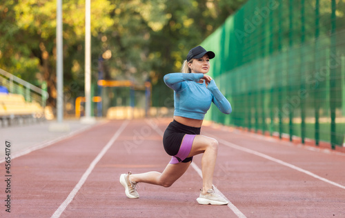 Athletic woman practicing lunges with fitness rubber bands in the stadium