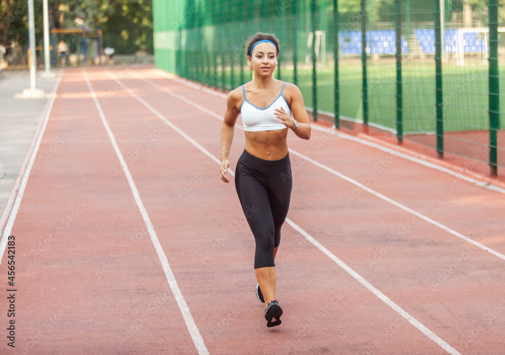 Beautiful muscular woman with perfect body in sports wear jogging in the stadium in the early morning