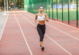 Beautiful muscular woman with perfect body in sports wear jogging in the stadium in the early morning