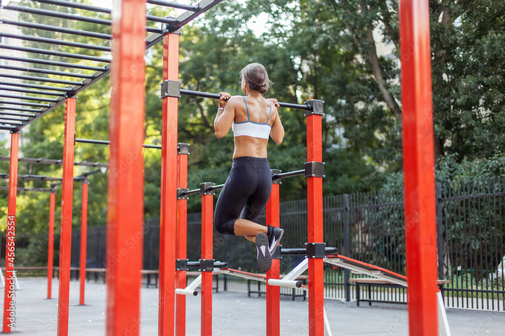 Young muscular woman pulls herself up on the horizontal bar on the workout ground