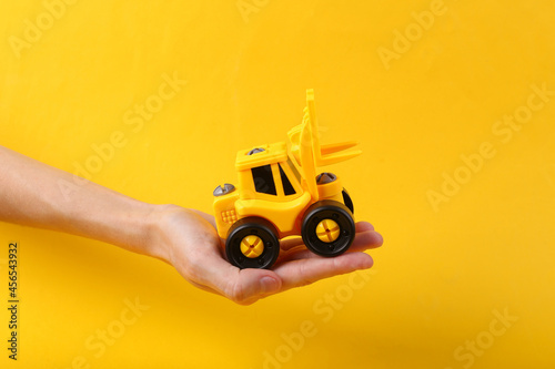 Toy forklift on a palm, yellow background