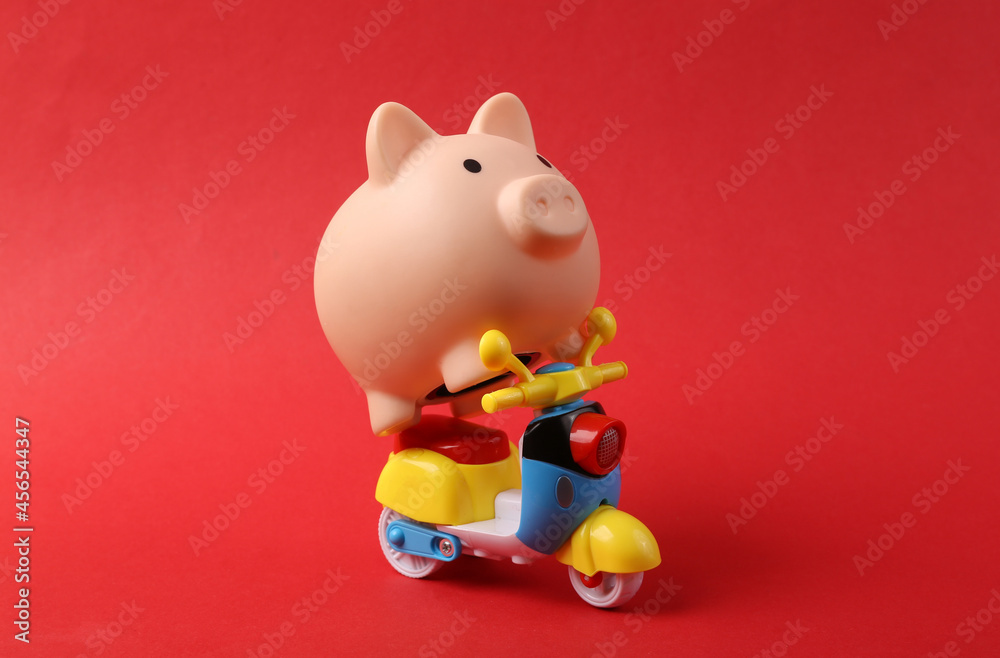 Piggy bank riding small scooter. Red background Piggy bank riding small scooter. Red background