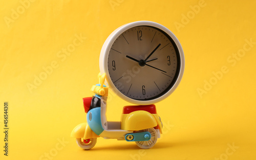 Toy scooter with alarm clock on yellow background. Delivery concept photo