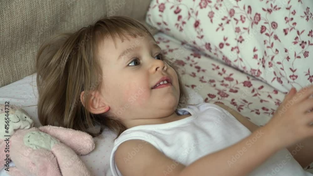 Little baby girl lies on bed waking up in morning takes bottle of milk and sucks. Child drinks infant formula. Baby food concept Little baby girl lies on bed waking up in morning takes bottle of milk and sucks. Child drinks infant formula. Baby food concept
