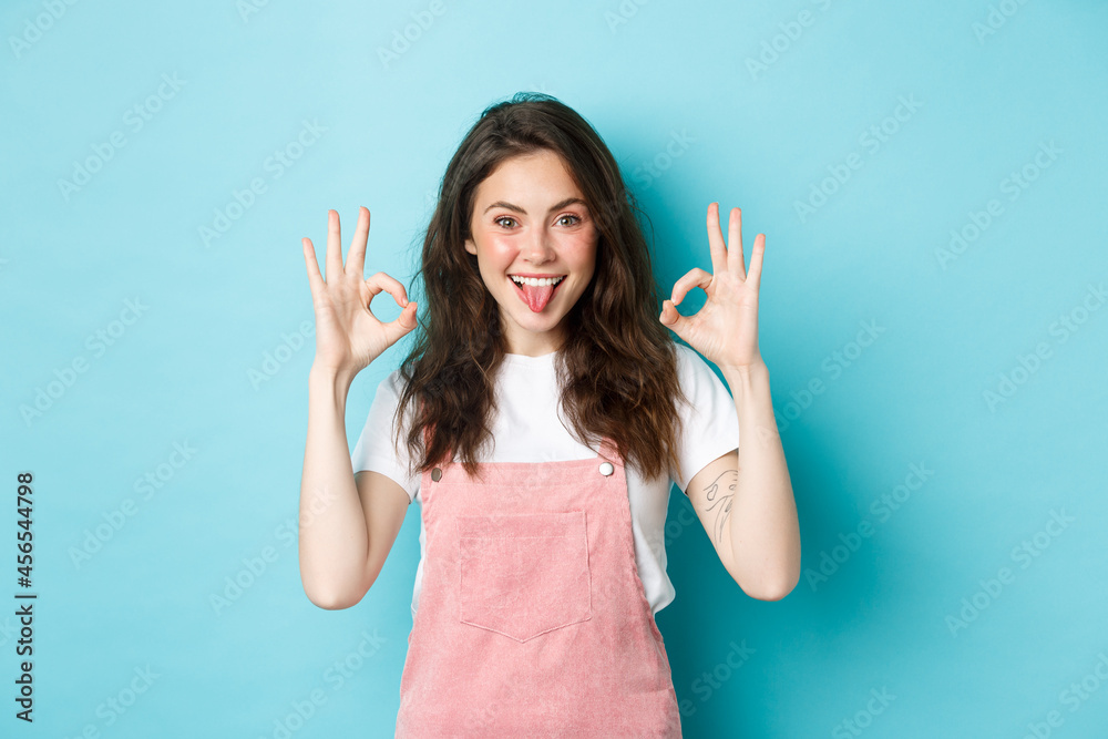 Portrait of excited brunette girl with curly hairstyle, showing okay signs,  praise perfect choice, recommend good thing, give OK sign, standing over  blue background Stock Photo | Adobe Stock