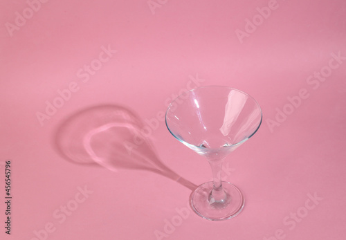 Minimalistic shot of empty cocktail glass with long trending shadow on pink background