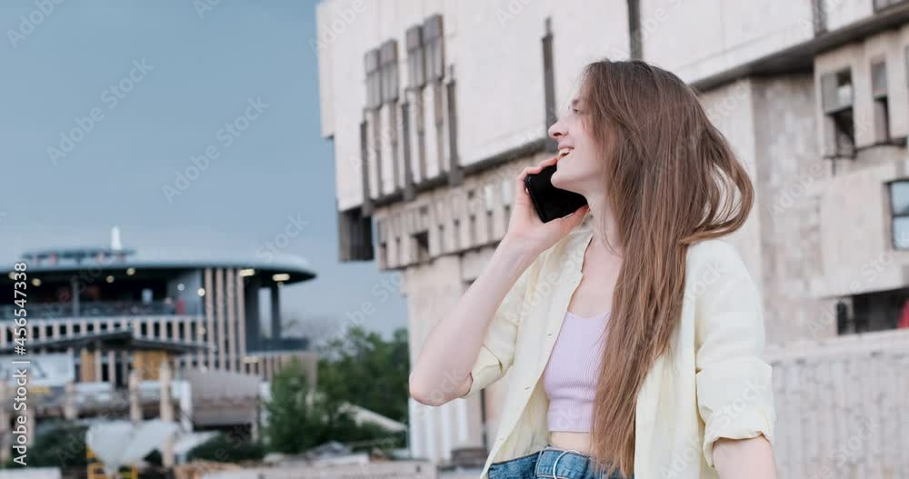 Young woman on balcony is talking on phone and correcting her hair. Girl with long hair takes phone call. Young woman on balcony is talking on phone and correcting her hair. Girl with long hair takes phone call.