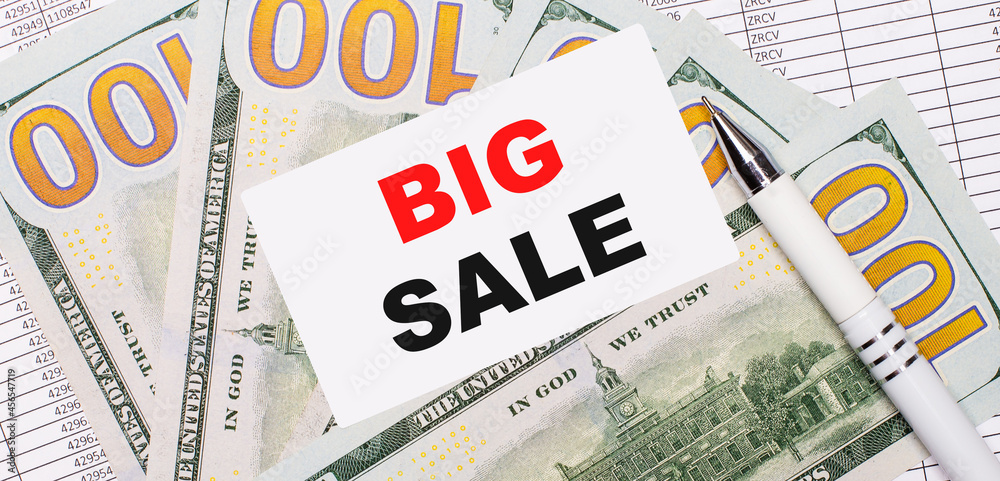 Against the background of reports and dollars - a white pen and a card with the text BIG SALE. Business concept