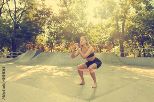 Beautiful young fit woman doing morning exercise with fitness rubber bands outdoors. © splitov27
