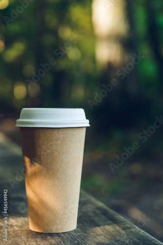 Small cardboard blank takeaway coffee cup on bench in forest. Walking with hot drink.
