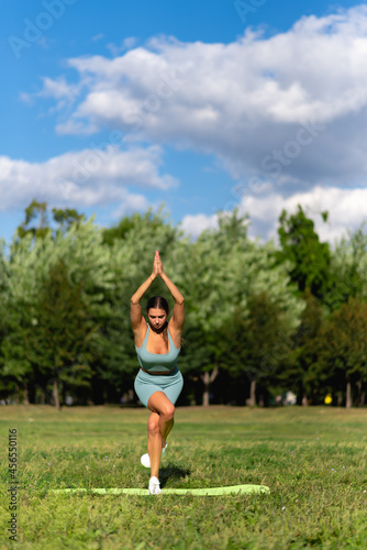 A beautiful sportive girl is engaged in yoga on green grass in a city park. Prapadasana pose © Granmedia