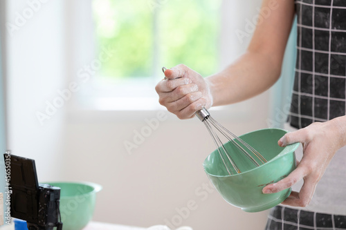 close up woman blogger making a bread, whisking something in a bowl and recording stream live video online from camera photo