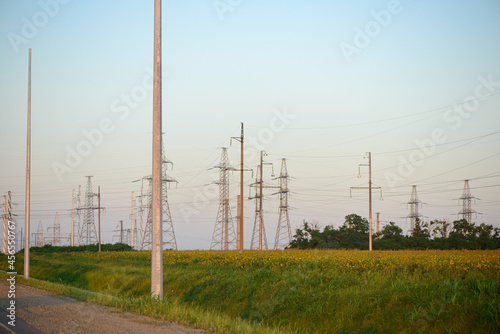 Poles and towers with power lines in the middle of a green field on a summer evening