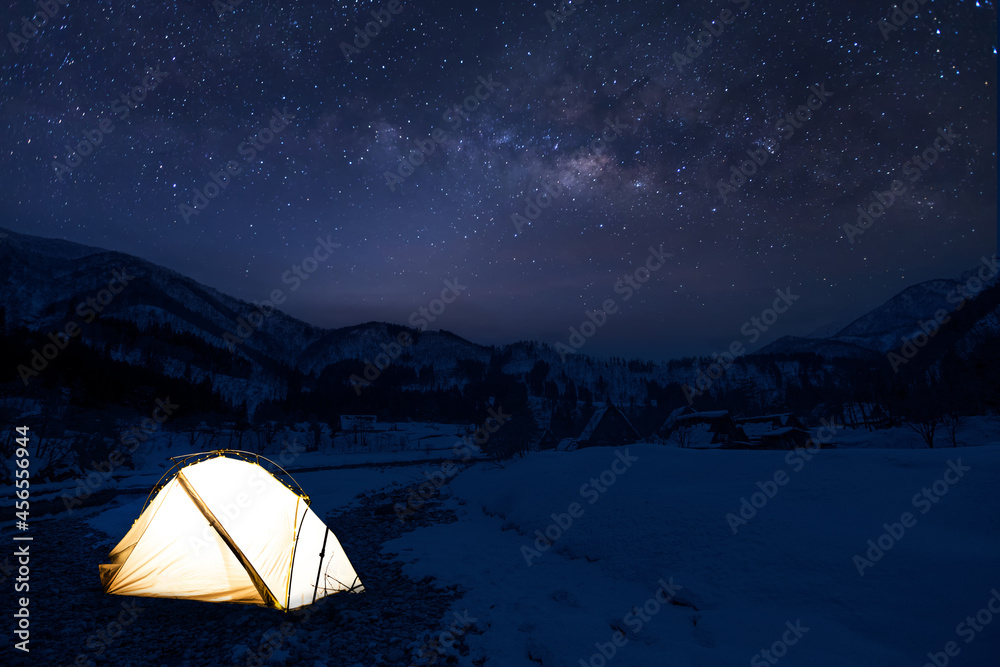 Camping in the wilderness. A pitched tent under the glowing night sky stars of the milky way with snowy mountains. Milky Way and Mount Baker, white tent in foreground