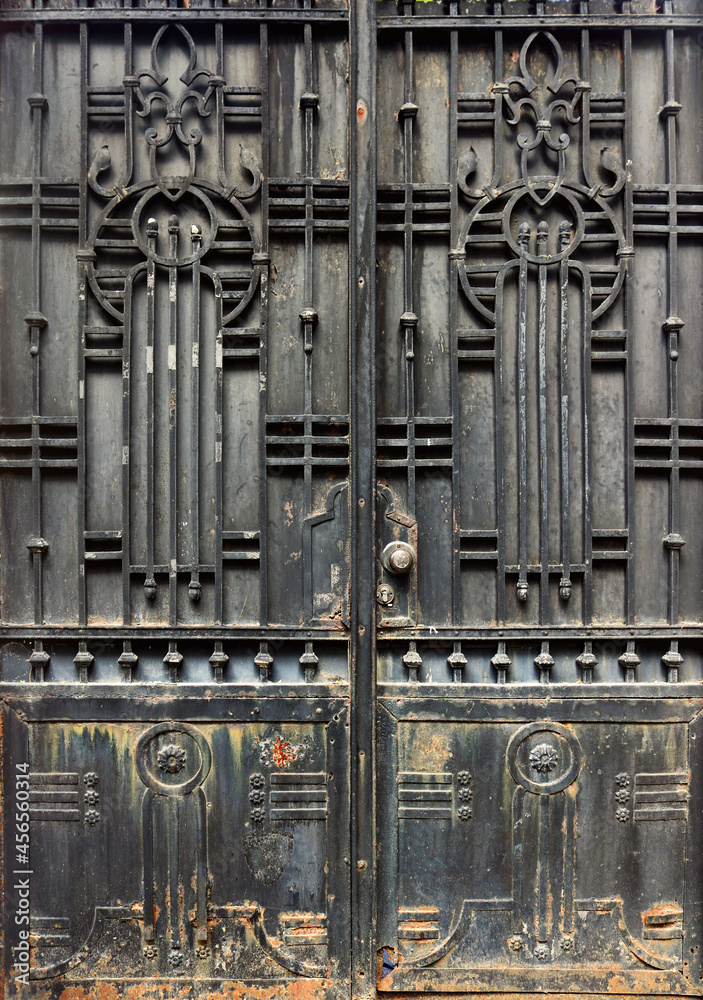 black metallic ornate door decorated in the art neuveau style -- worn steam punk dark surface with dirty and weathered background