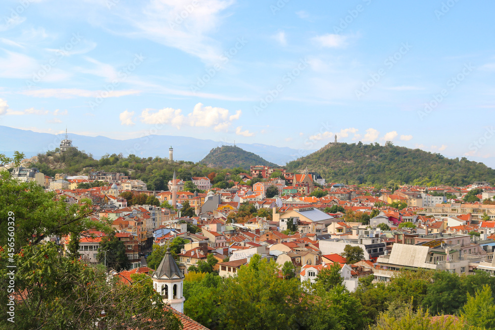 Tourist postcard of the ancient Plovdiv in Bulgaria with a panoramic view of the city with buildings and monuments, trees, hills and mountains in the background, with a blue sky with clouds