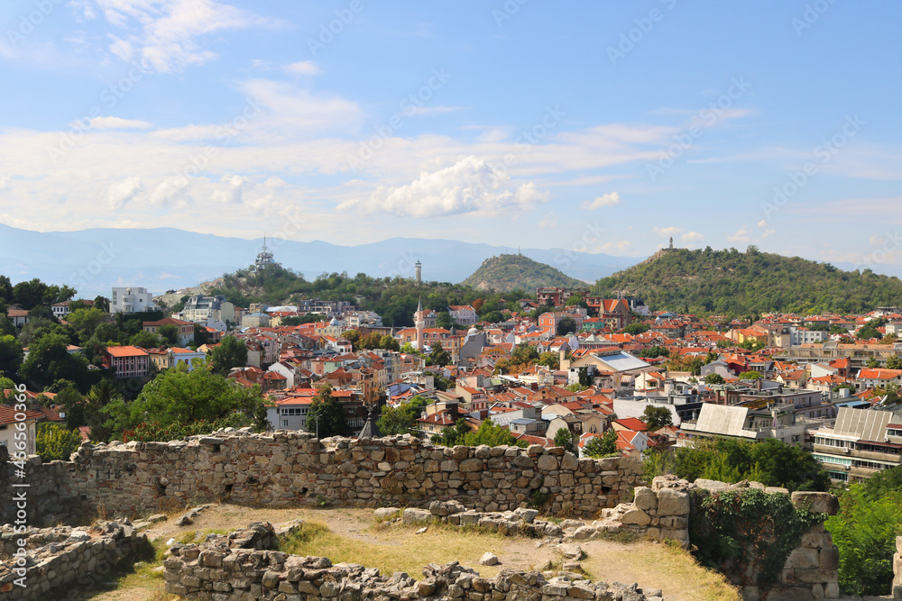 Tourist postcard of Plovdiv in Bulgaria with the Thracian ruins of Nevet Tepe and a panoramic view of the city in the background, with monuments, hills, mountains and a blue sky with clouds