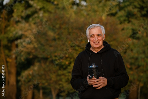 Mature man drinking water after jogging in autumn park during sunset   